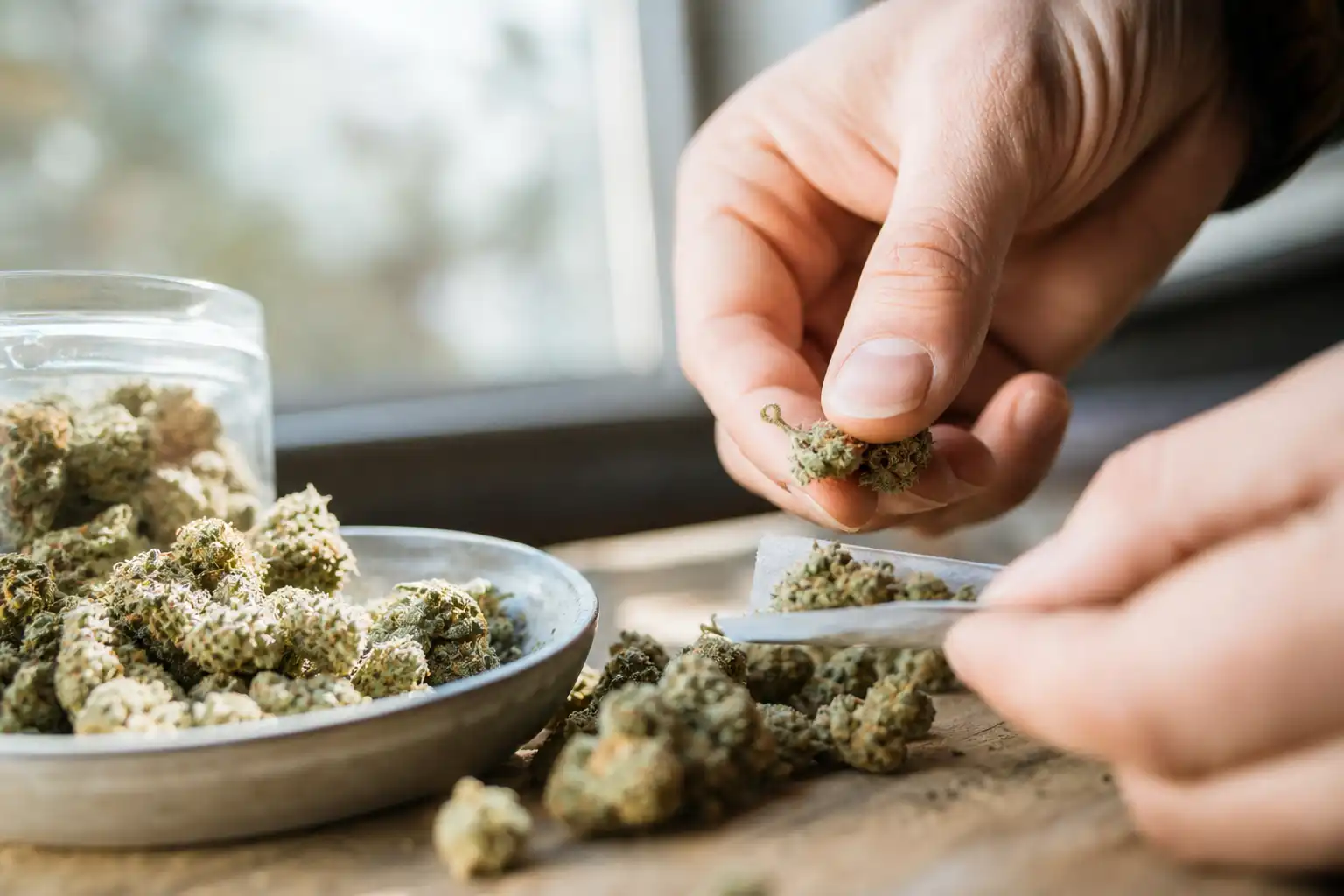 Des mains préparent quelque chose, autour de cannabis médical troisième, près d'une fenêtre.